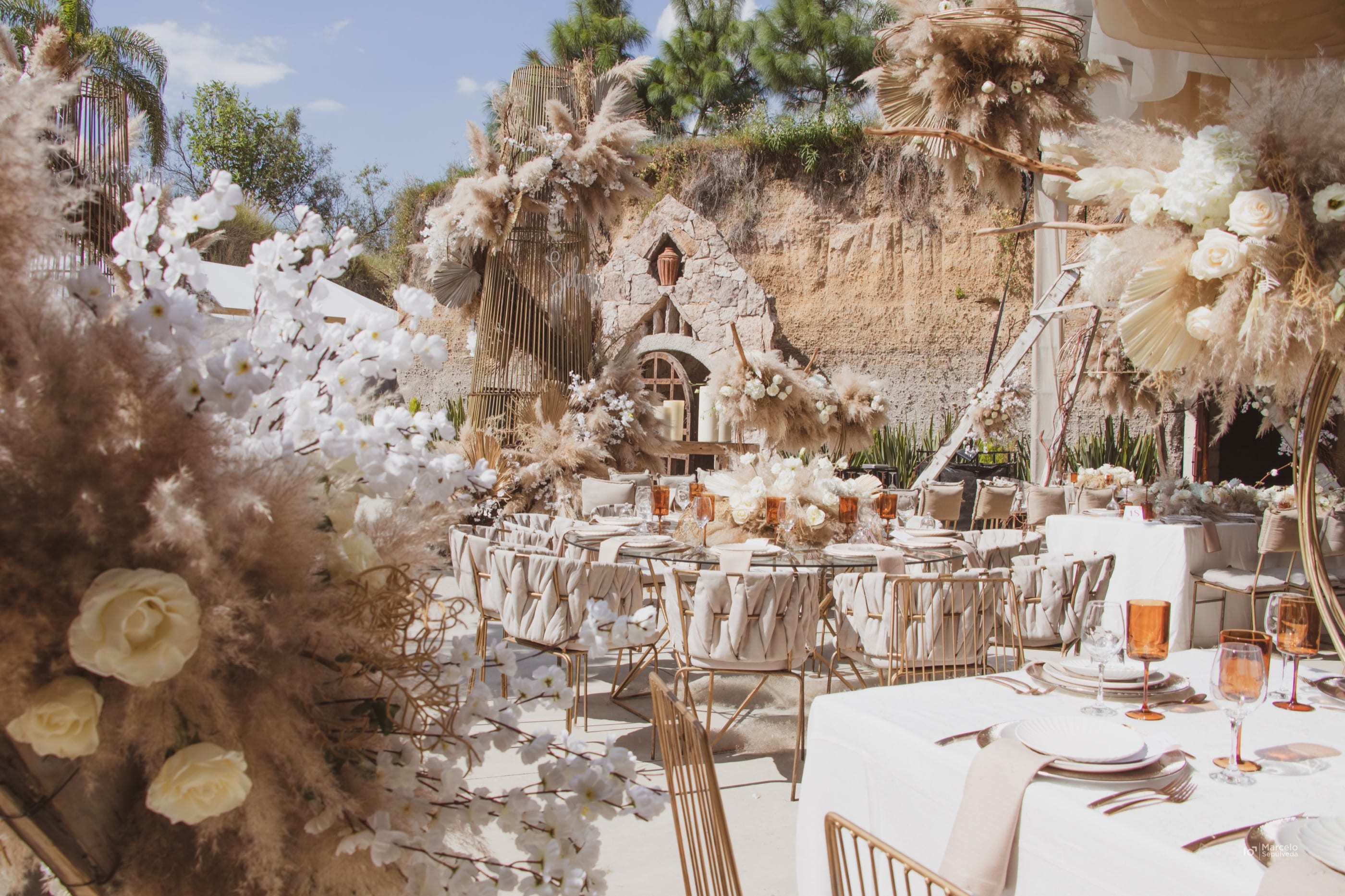 Montaje al aire libre con pampa seca, flores blancas y mesas de banquete, producido por Castella Eventos