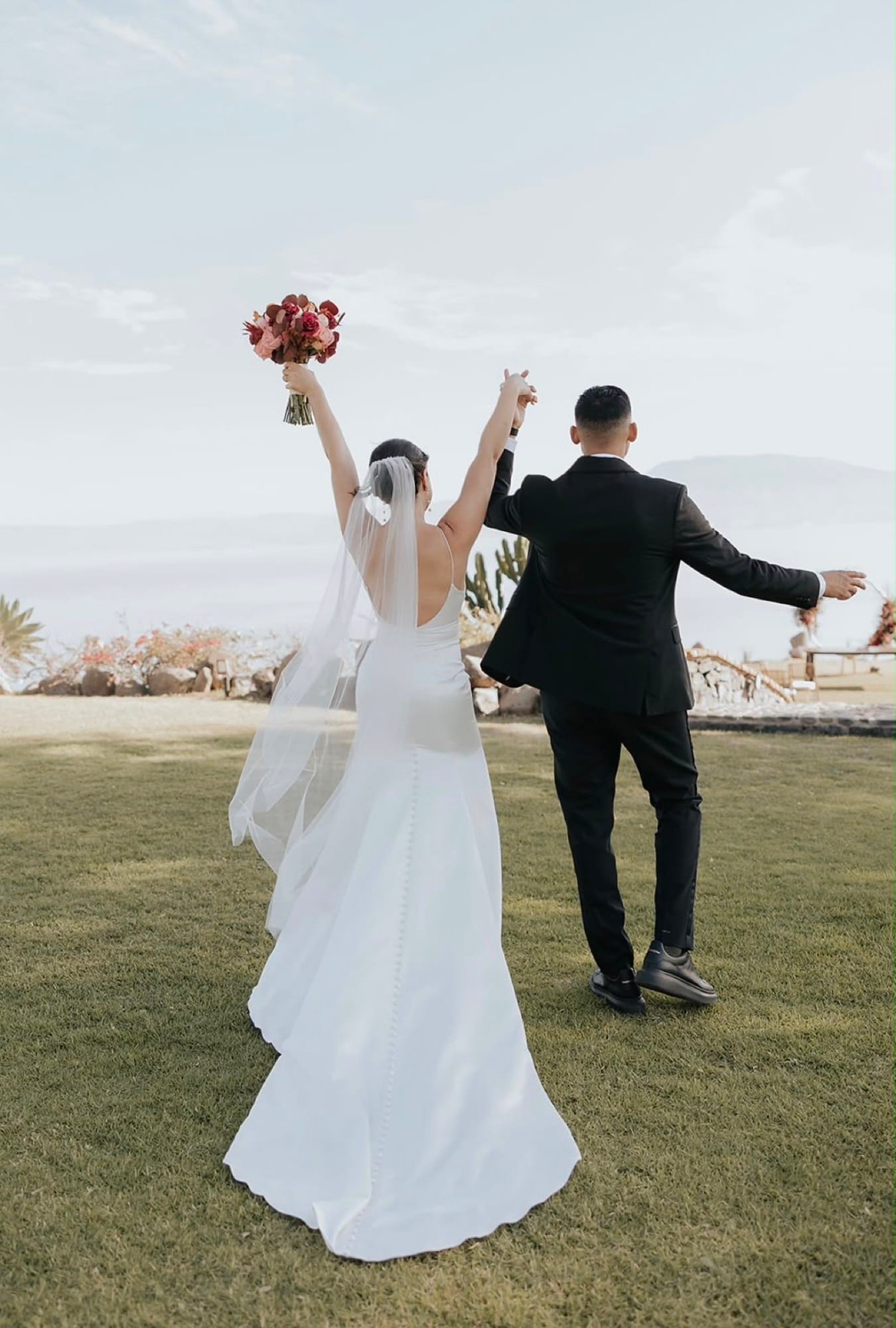 Novios celebrando con los brazos en alto frente al lago