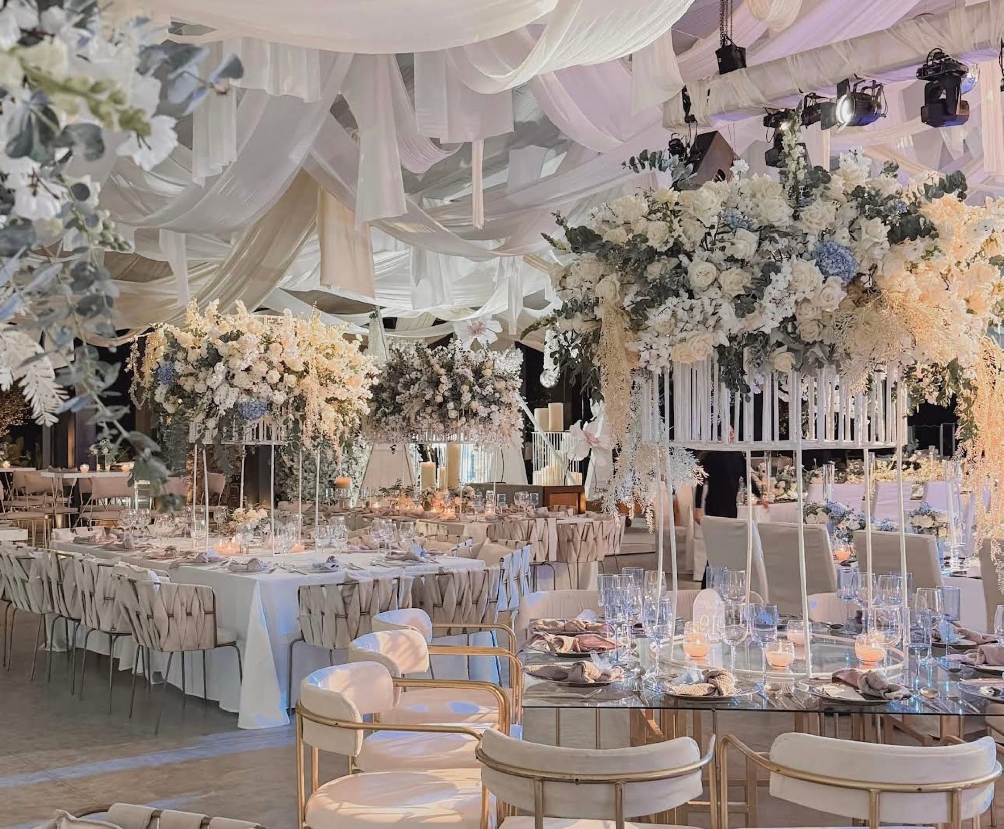 Salón de XV años con techo drapeado en blanco y centros de mesa de flores blancas y azules