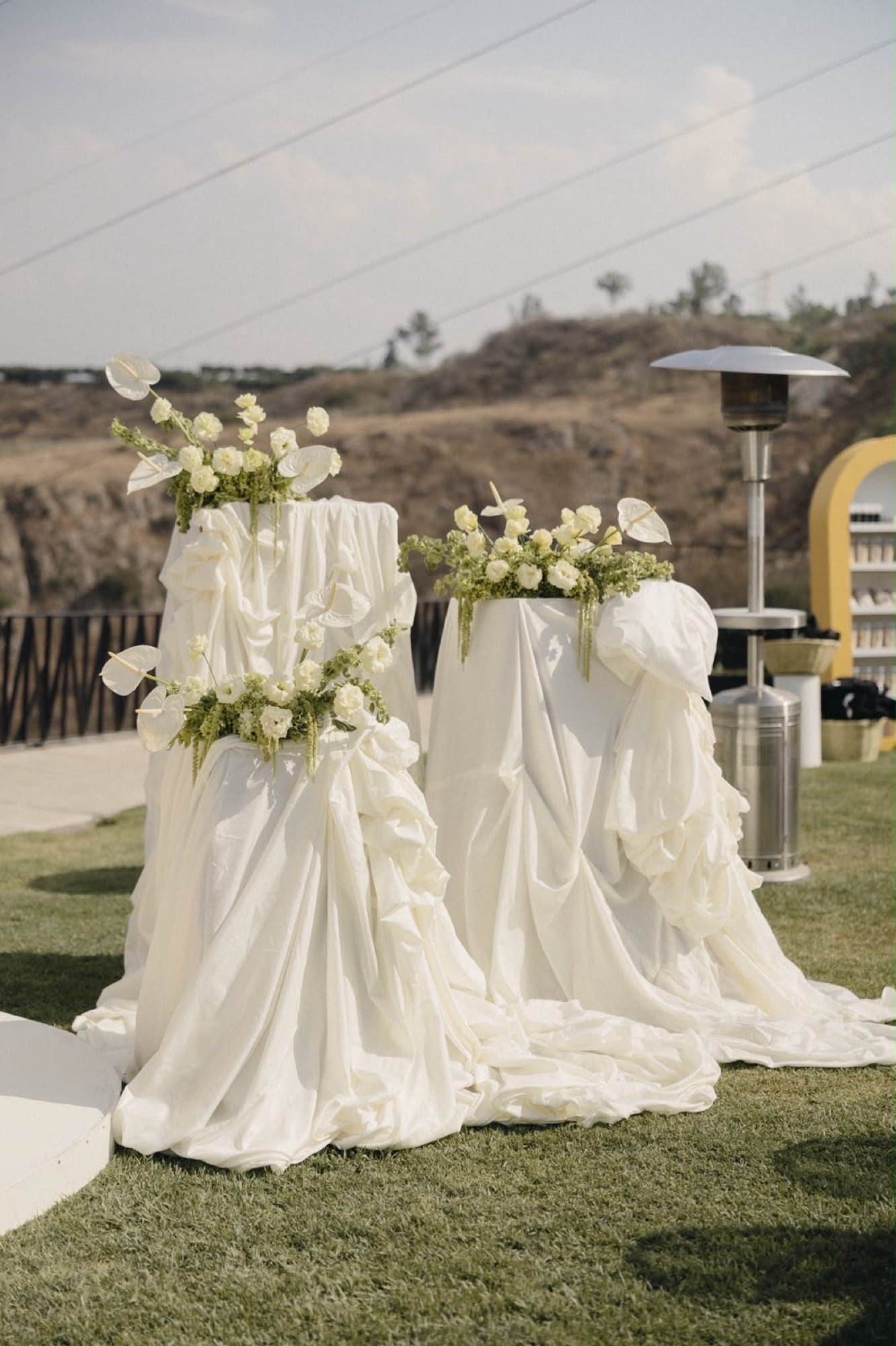 Pedestales con telas blancas drapeadas y flores para una ceremonia al aire libre