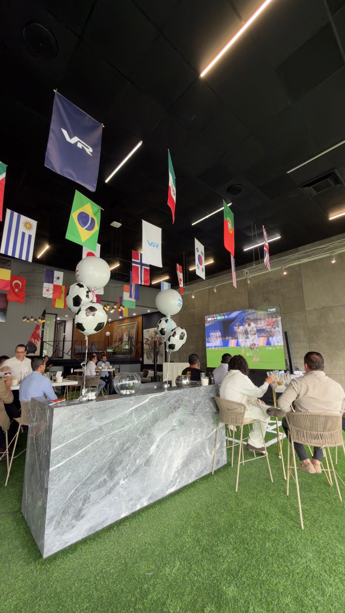 Evento corporativo con barra de mármol, pantalla y banderas colgantes